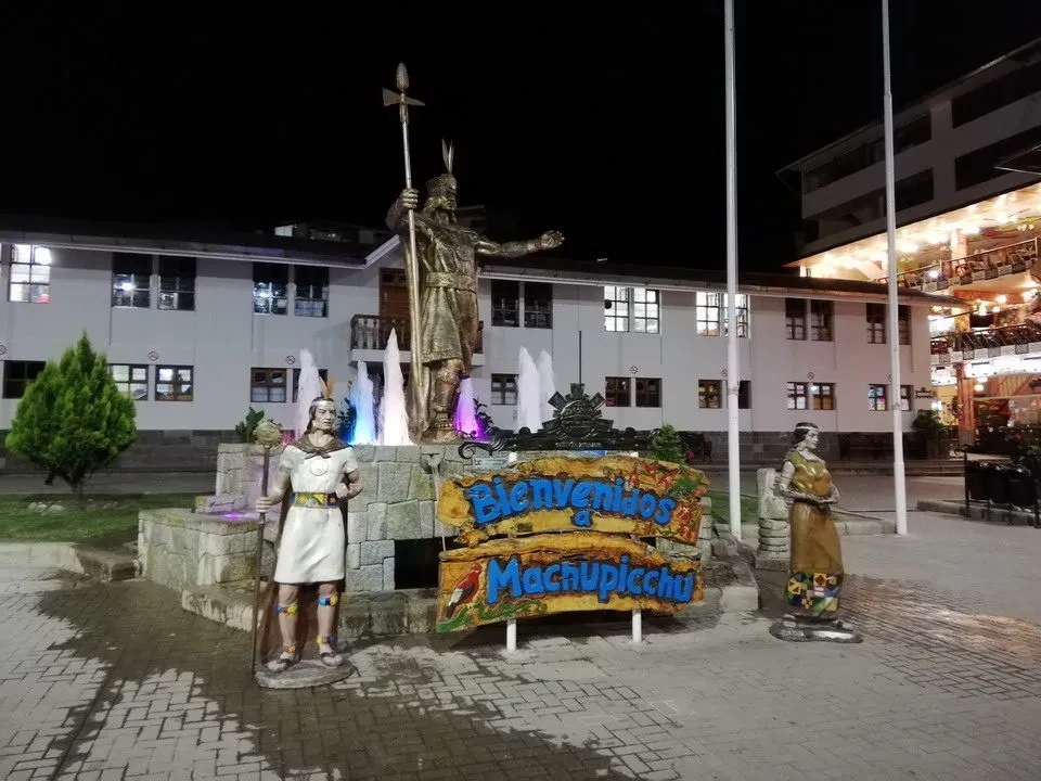 Una statua di Cristo con una figura femminile davanti a un cartello festivo in una piazza.