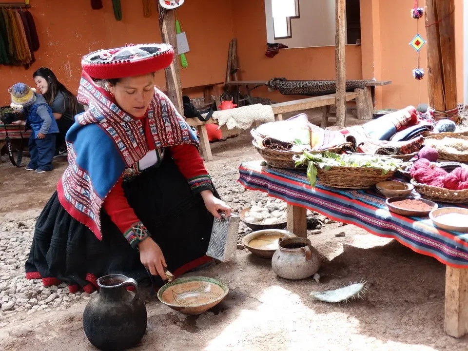 Una donna indiana siediti lavora artigianato in un contesto rurale peruviano o boliviano.