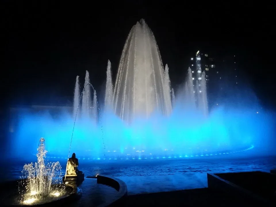 Fontane illuminate di blu riflettono l'acqua in una scena notturna.