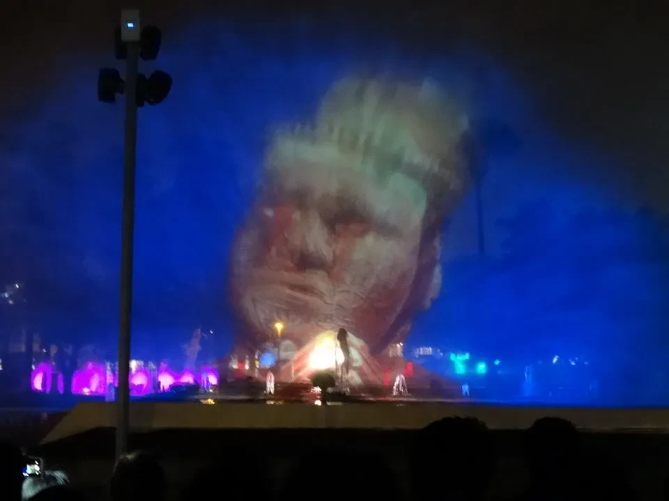 Una grande scultura raffigura una figura umana illuminata da luci blu e rosse in un evento notturno.