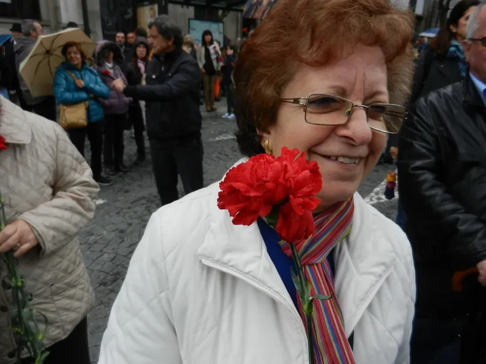Donna sorridente con un fiore rosso in una folla stradale a Porto.