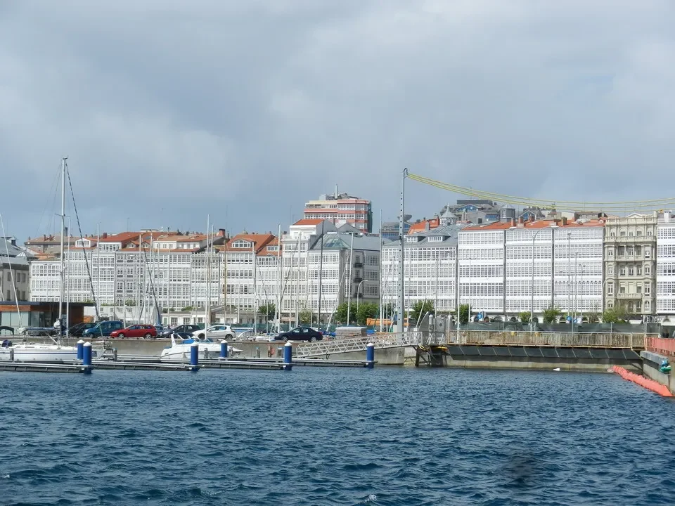 Vista di una città portuale con edifici lungo la riva e imbarcazioni in primo piano.