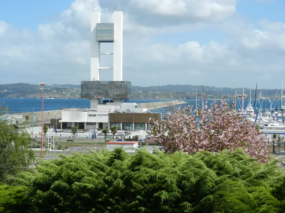 Una vista panoramica di un porto con una struttura bianca prominente e vegetazione lussureggiante in primo piano. Una vista panoramica di un porto con una struttura bianca prominente e vegetazione lussureggiante in primo piano.