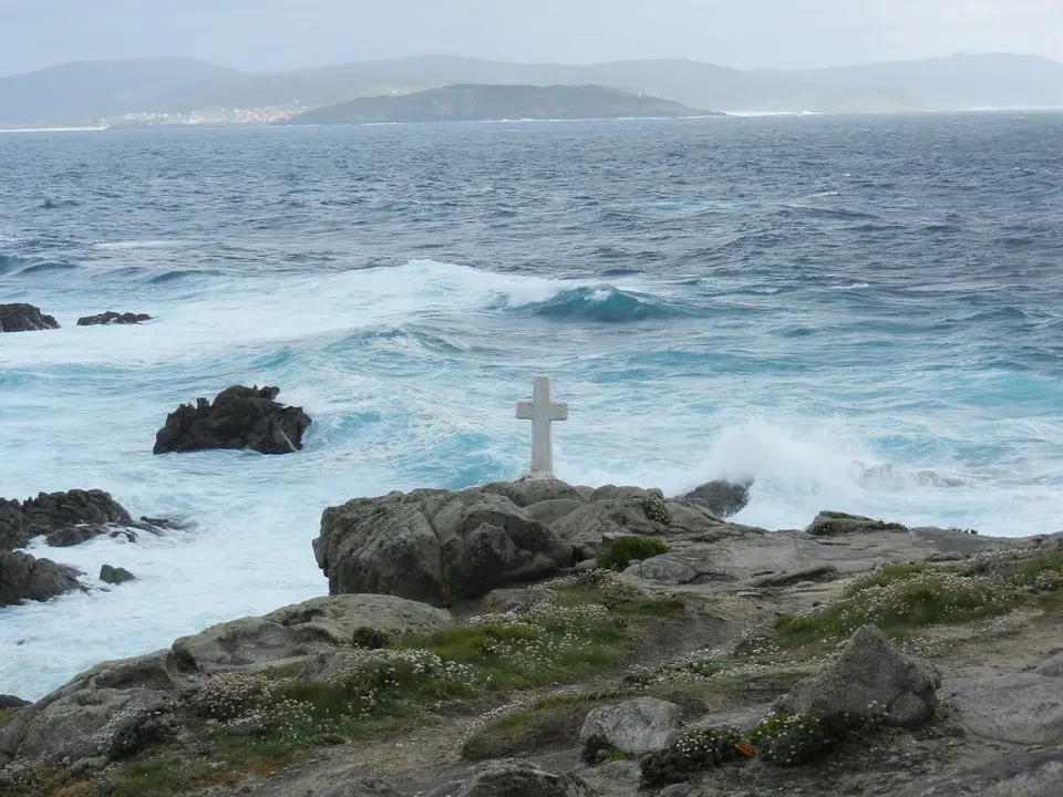 Una croce in pietra si erge su una roccia battuta dalle onde del mare.