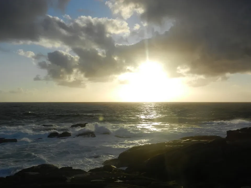Tramonto drammatico sul mare con onde che si infrangono sulle rocce.