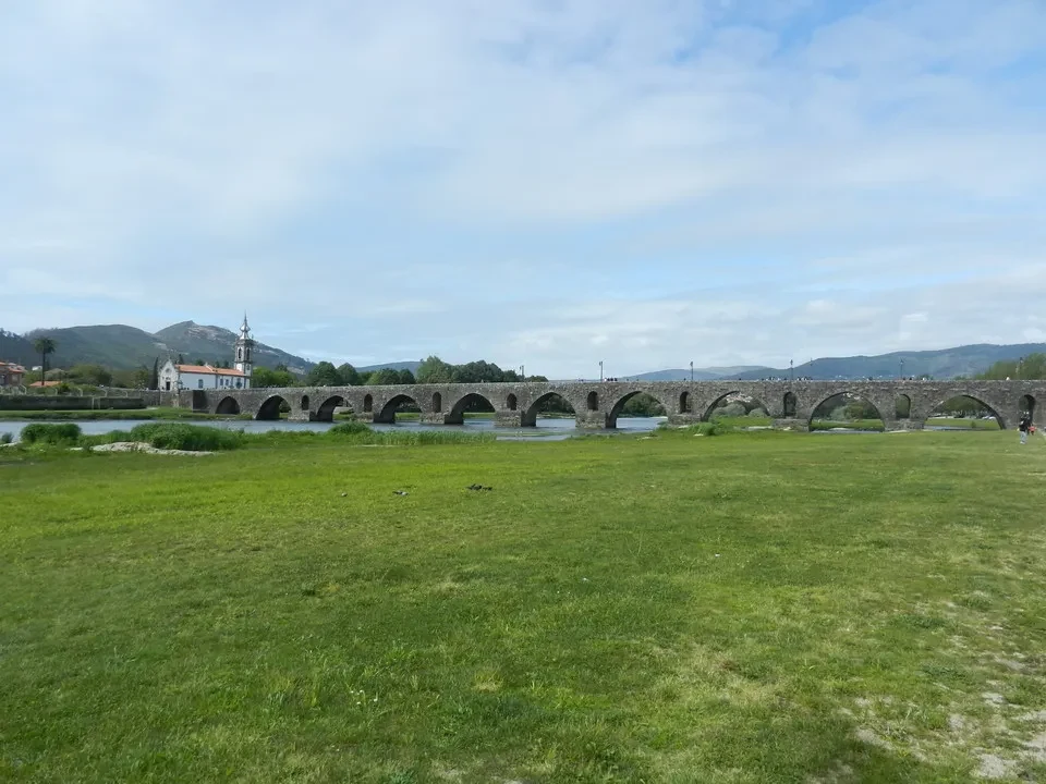 Un lungo ponte in pietra attraversa un fiume verde con un paesaggio collinare sullo sfondo.