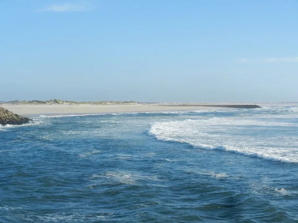 Onde blu e sabbia bagnata si incontrano sotto un cielo sereno in Portogallo.