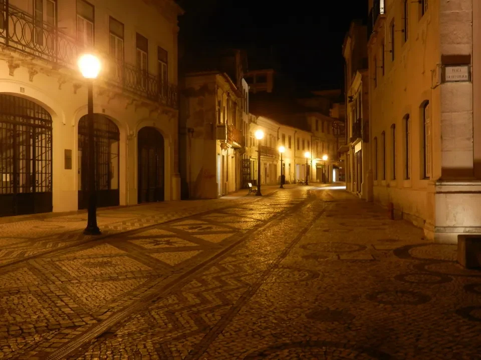 Una strada acciottolata e illuminata di lanterne in una città portoghese al tramonto.