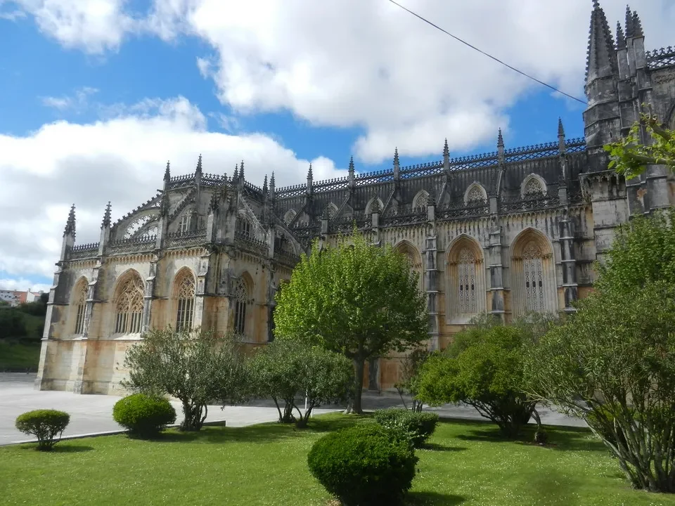 Mosteiro da Batalha in Portugal with a green lawn and blue sky above.
