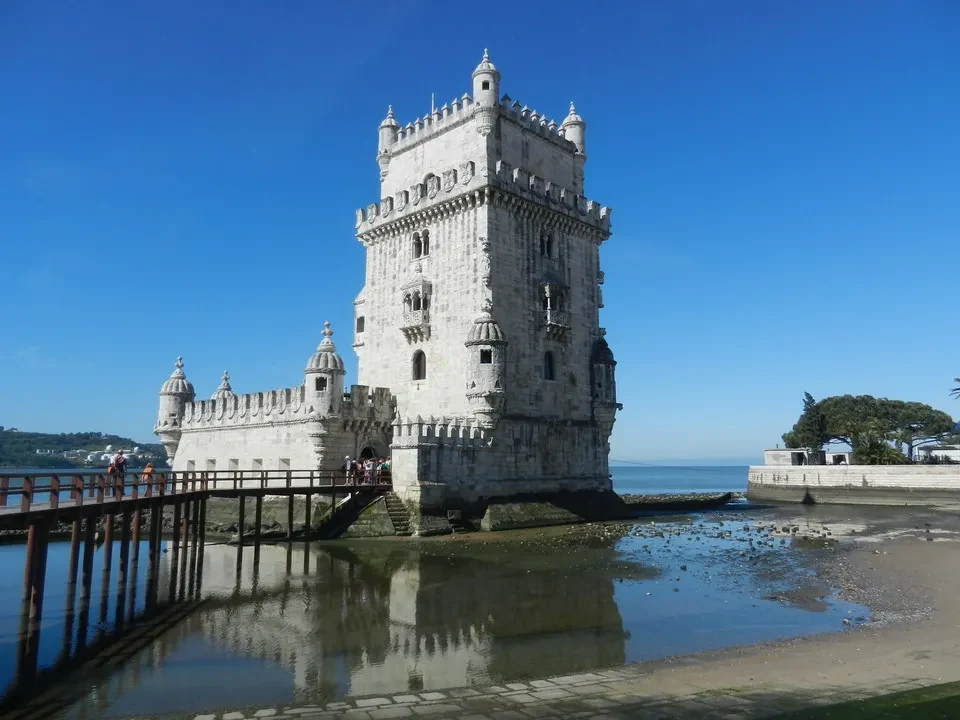 A large white fortress sits on a stone pier by the water.