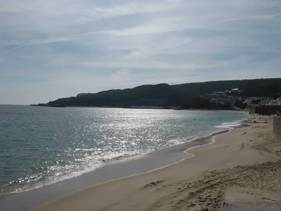 Una spiaggia sabbiosa si estende lungo la costa con il mare e le colline sullo sfondo.