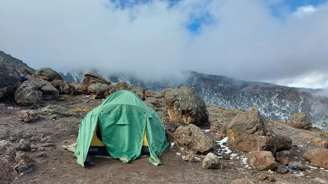 Una tenda verde è posizionata su un terreno roccioso in un paesaggio montano nuvoloso.