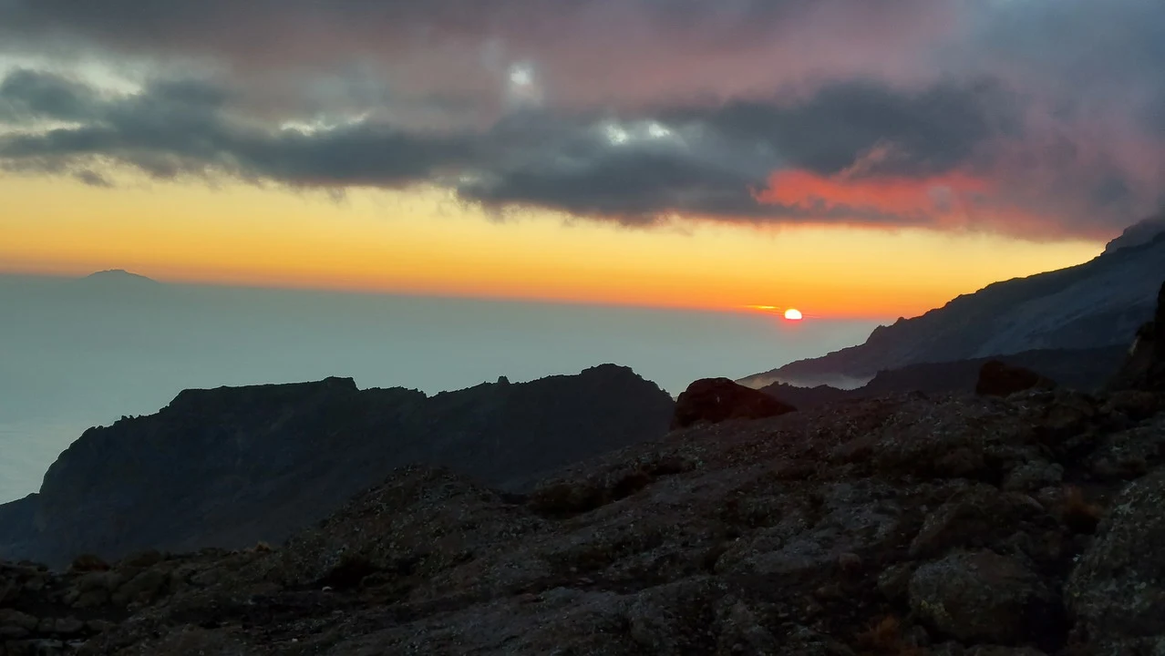 Paesaggio montano drammatico all'alba o al tramonto con nuvole colorate sopra le vette.