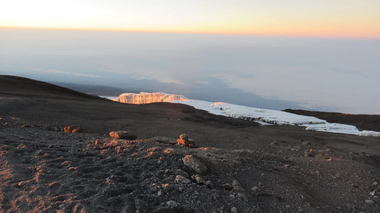 La cima del Kilimangiaro è visibile all'alba sopra un paesaggio montano.