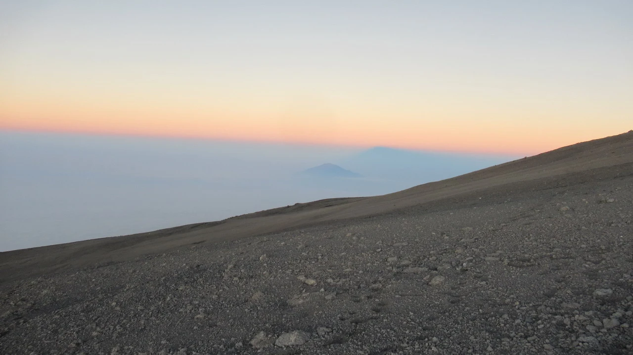 Pendio roccioso del Kilimanjaro al tramonto sopra un mare di nuvole.