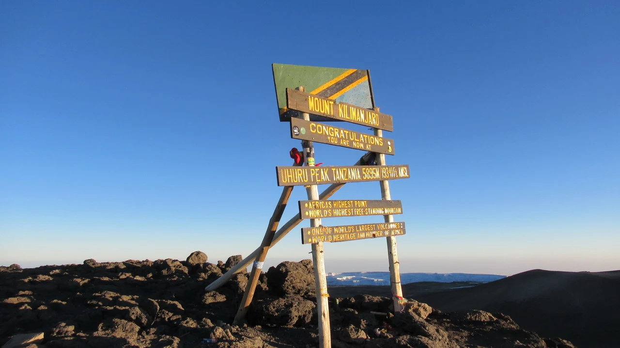 Vista panoramica dalla cima del Monte Kilimanjaro con un cartello di sentiero in primo piano.
