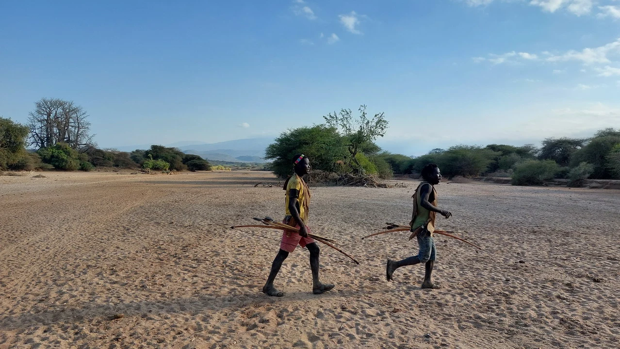 Due uomini camminano attraverso un paesaggio secco africano con vegetazione rada. Due uomini camminano attraverso un paesaggio secco africano con vegetazione rada.
