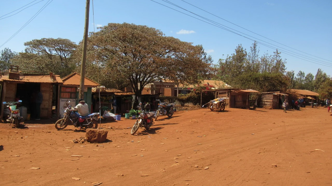 Una veduta di un'area rurale in Tanzania con strutture semplici e persone in primo piano.