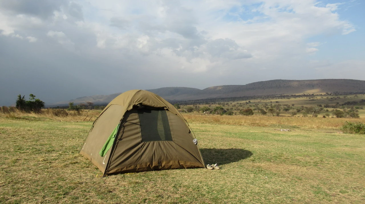 Una tenda da campo è posizionata su un prato aperto con un paesaggio africano sullo sfondo.