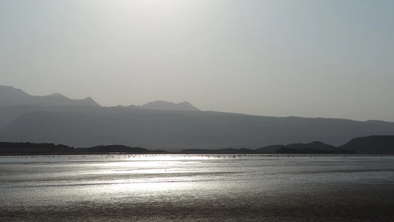 Vasta distesa d'acqua riflette la luce solare tra montagne lontane.