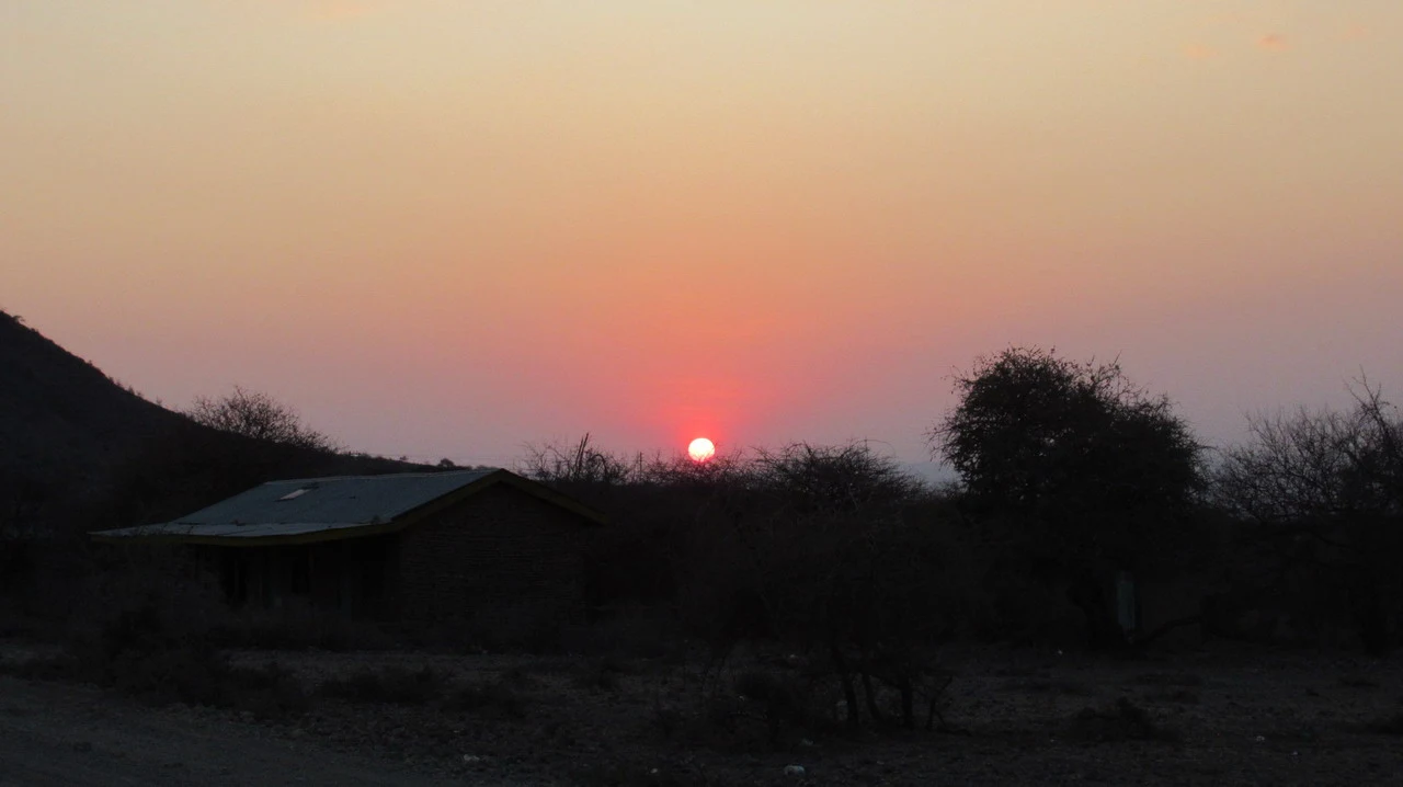 Tramonto su un paesaggio africano con una piccola abitazione in primo piano.