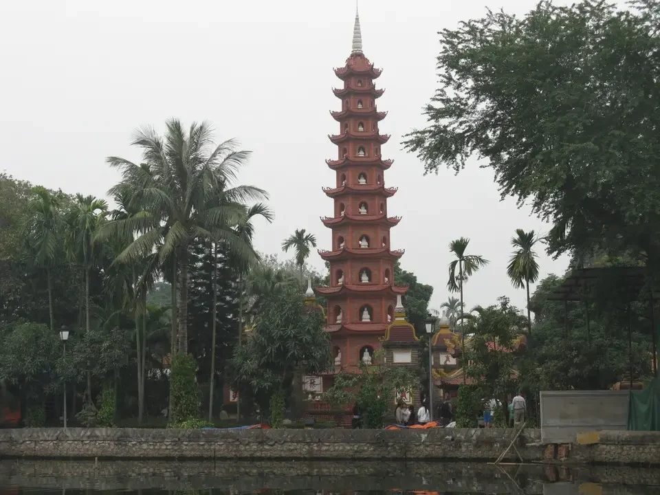 Una pagoda rossa in legno si erge sopra un corpo d'acqua in un paesaggio tra Vietnam e Cambogia.