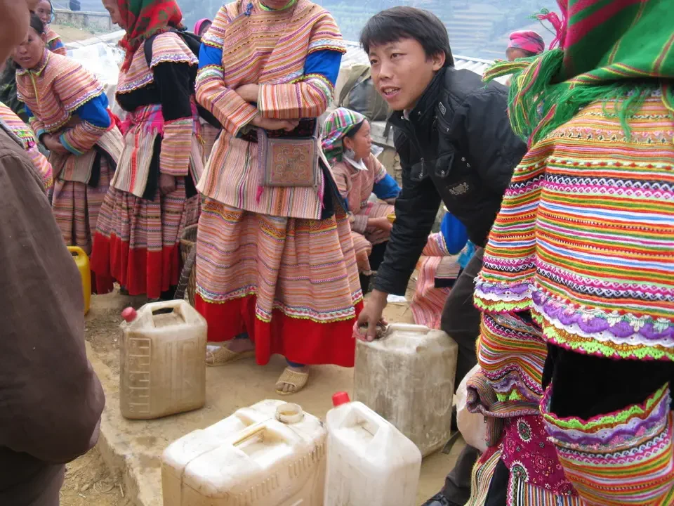 Persone in abiti tradizionali interagiscono con contenitori di plastica all'aperto.