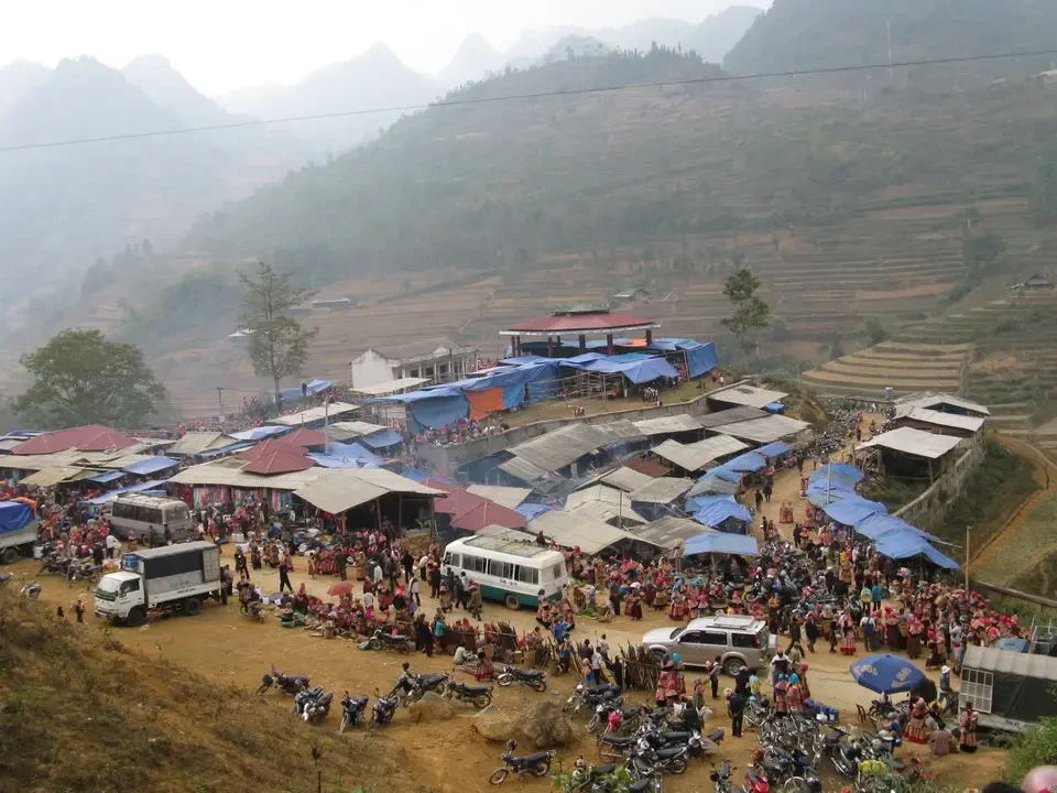 Un mercato affollato con bancarelle allestite in una valle montuosa del Vietnam o del Cambogia.