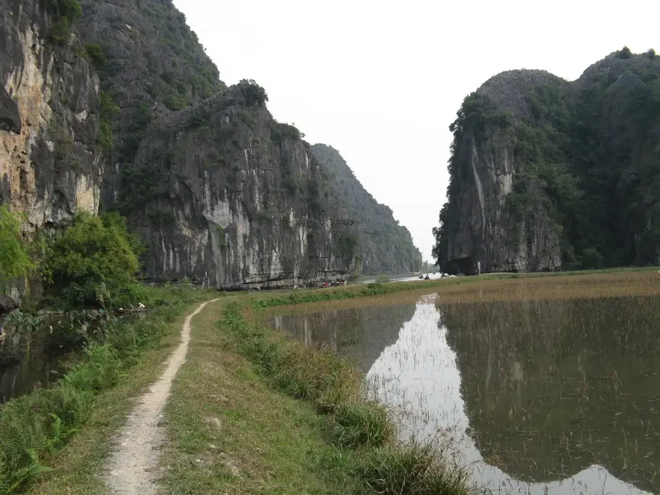 Sentiero sterrato lungo le scogliere verdi di un paesaggio fluviale tra Vietnam e Cambogia.