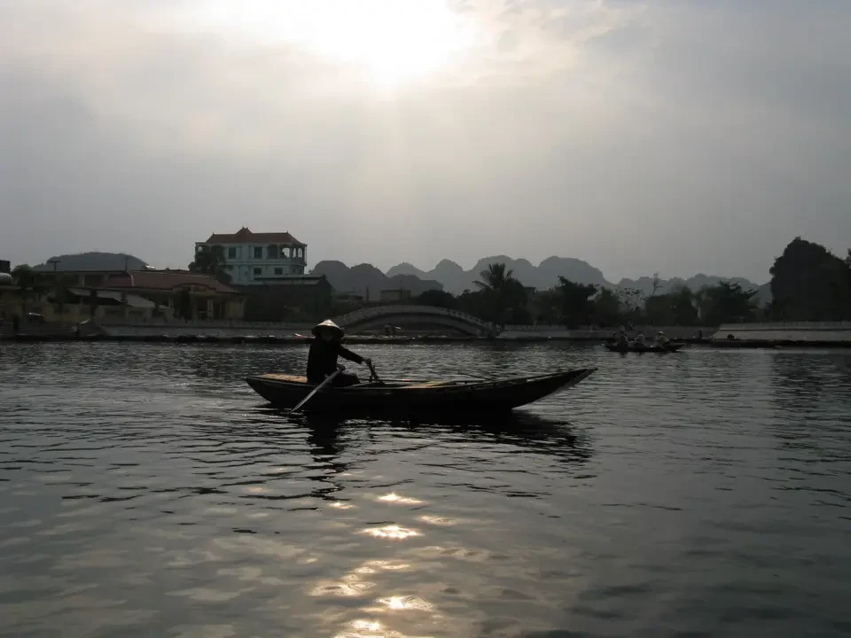 Una canoa naviga su un fiume con paesaggi di Vietnam e Cambogia sullo sfondo.