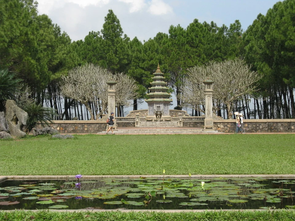 Una pagoda in pietra si trova in un giardino con alberi spogli e uno stagno in Vietnam o Cambogia.