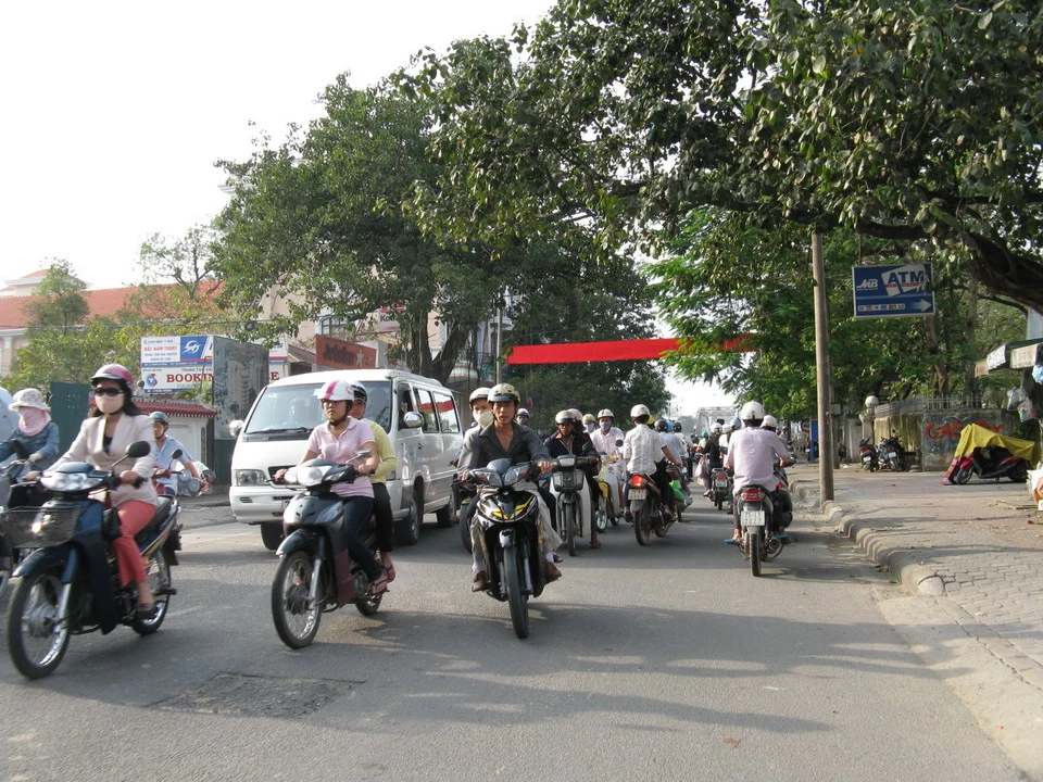 Un gruppo di motociclisti attraversa una strada alberata in Vietnam o Cambogia.