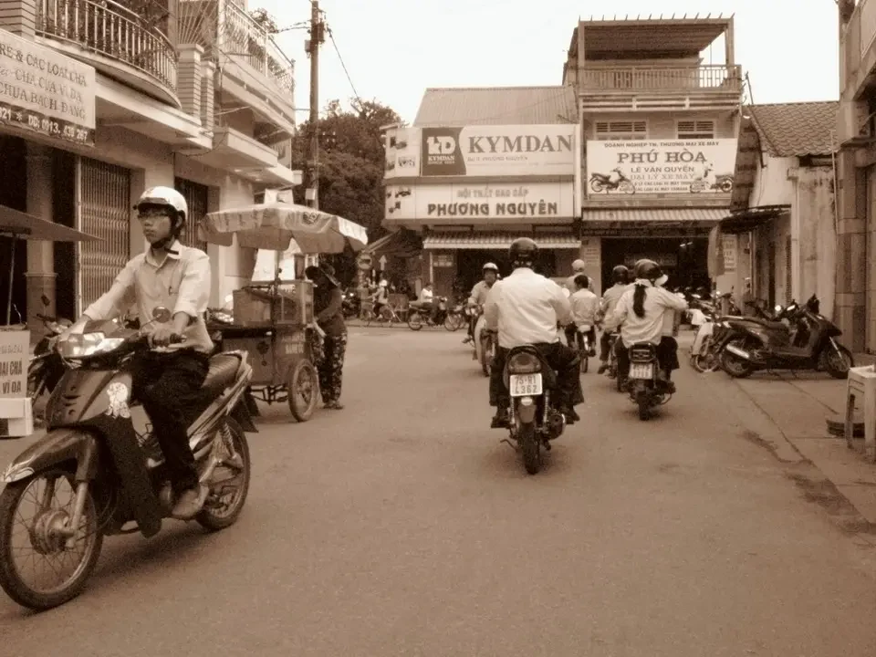 Un gruppo di motociclisti e persone attraversa una strada cittadina in Vietnam o Cambogia.