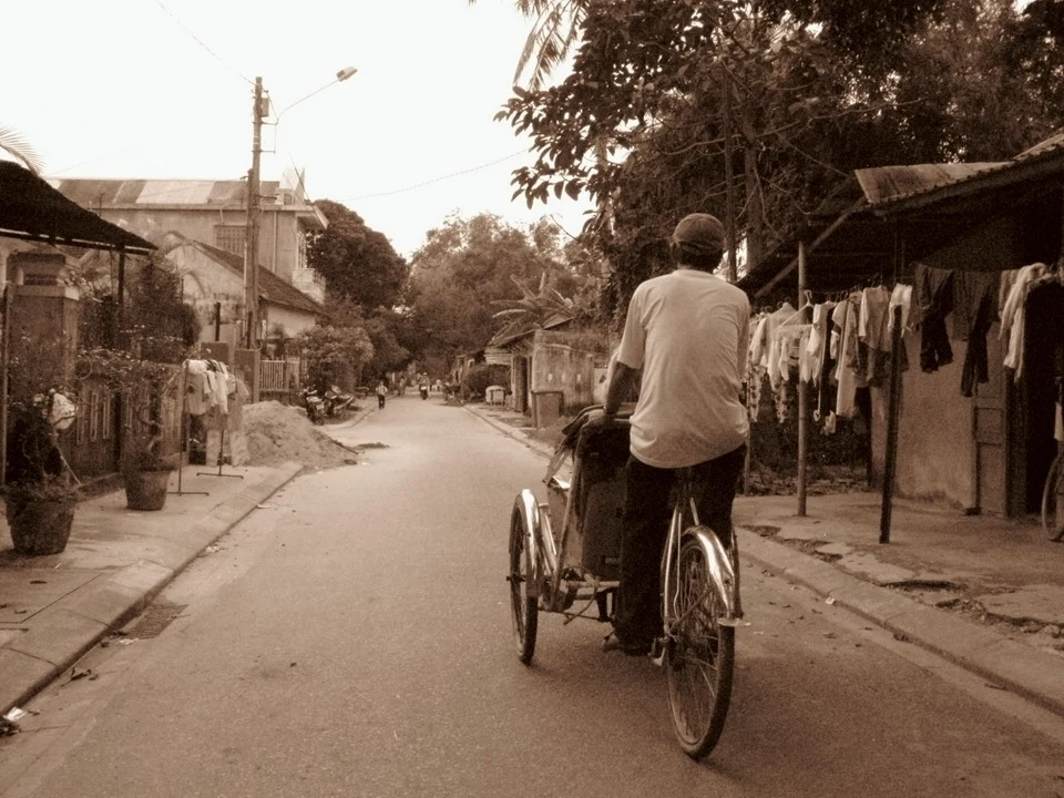 Un uomo pedala una bicicletta lungo una strada rurale in Vietnam o Cambogia con vestiti appesi.