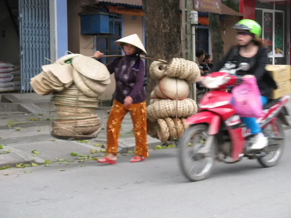 Due motociclist trasportano grandi quantità di paglia lungo una strada in Vietnam o Cambogia.