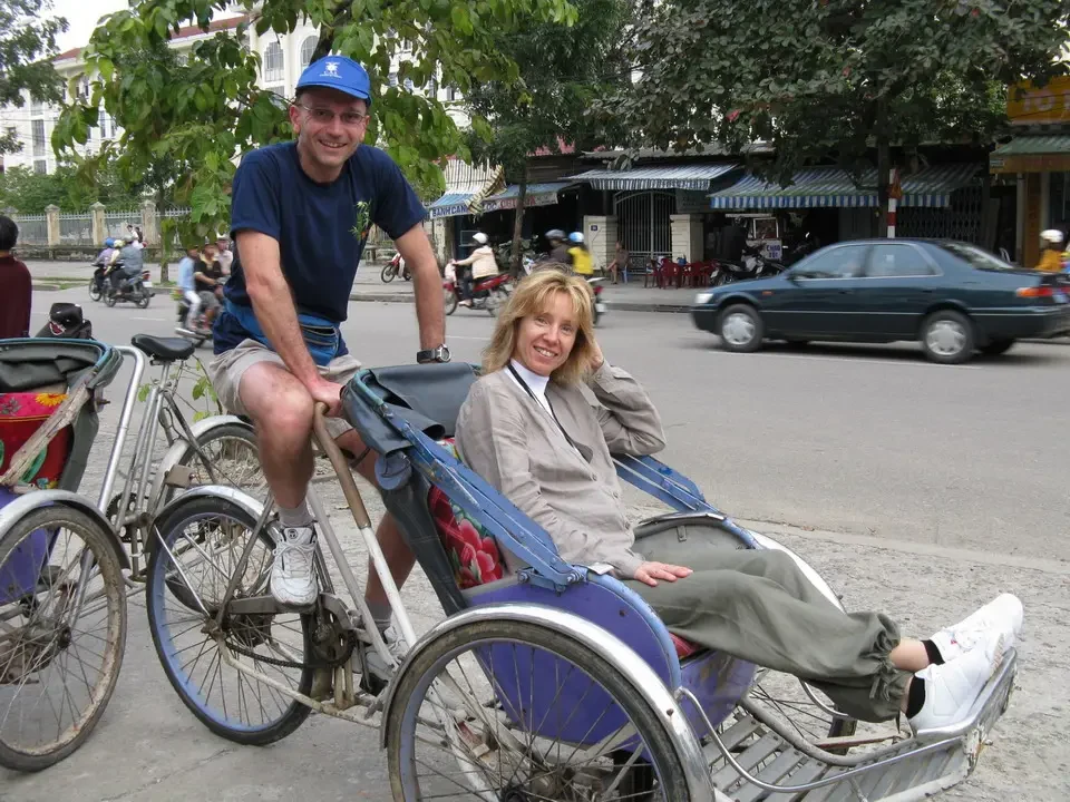 Due persone sorridono mentre guidano biciclette su una strada con edifici storici.