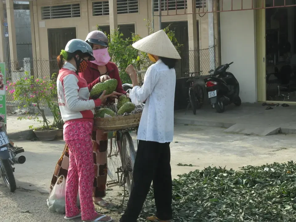 Tre persone stanno esaminando frutta su un mercato o in un'area esterna in Vietnam o Cambogia.