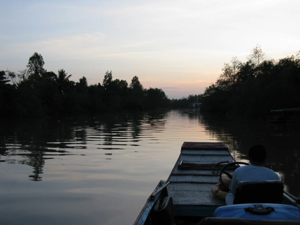 Tramonto sul fiume Mekong con vegetazione lussureggiante lungo le rive.