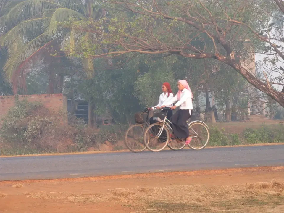Una donna pedala una bicicletta su una strada rurale in Vietnam o Cambogia.