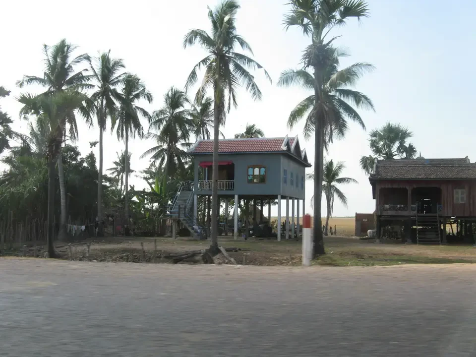 Una struttura in legno con tetto rosso si trova tra palme in un ambiente rurale del Vietnam o del Cambogia.