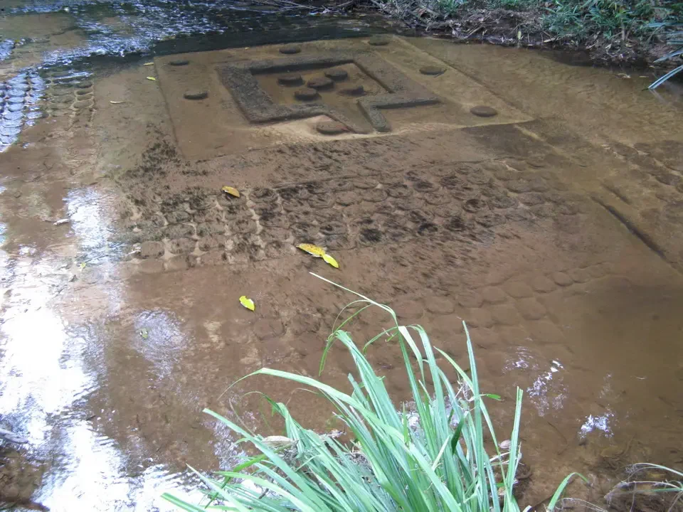 Un antico basamento in pietra è parzialmente sommerso dall'acqua fangosa di un ruscello.