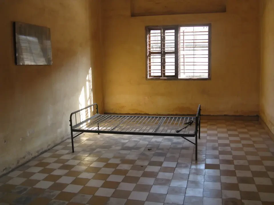 Interno di una stanza con pavimento a scacchi e una struttura in ferro battuto per il letto.