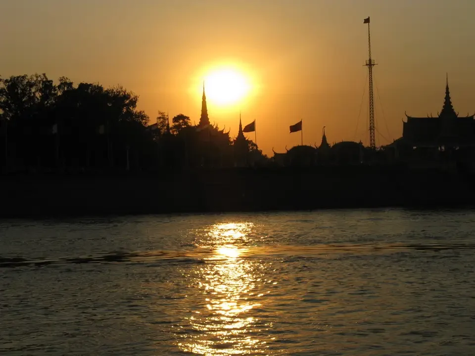 Tramonto dorato riflesso sull'acqua con silhouette di templi asiatici.