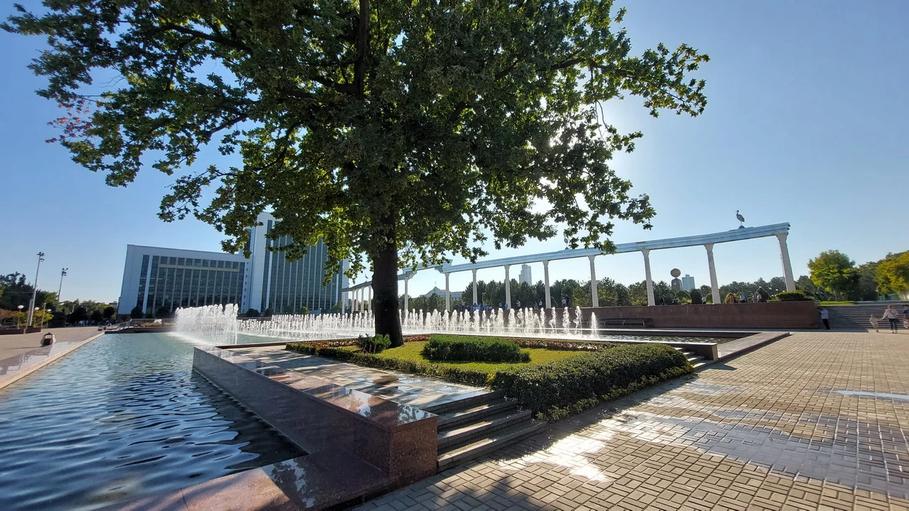 Il monumento all'Indipendenza di Tashkent in Asia Centrale con una fontana e alberi in primo piano.