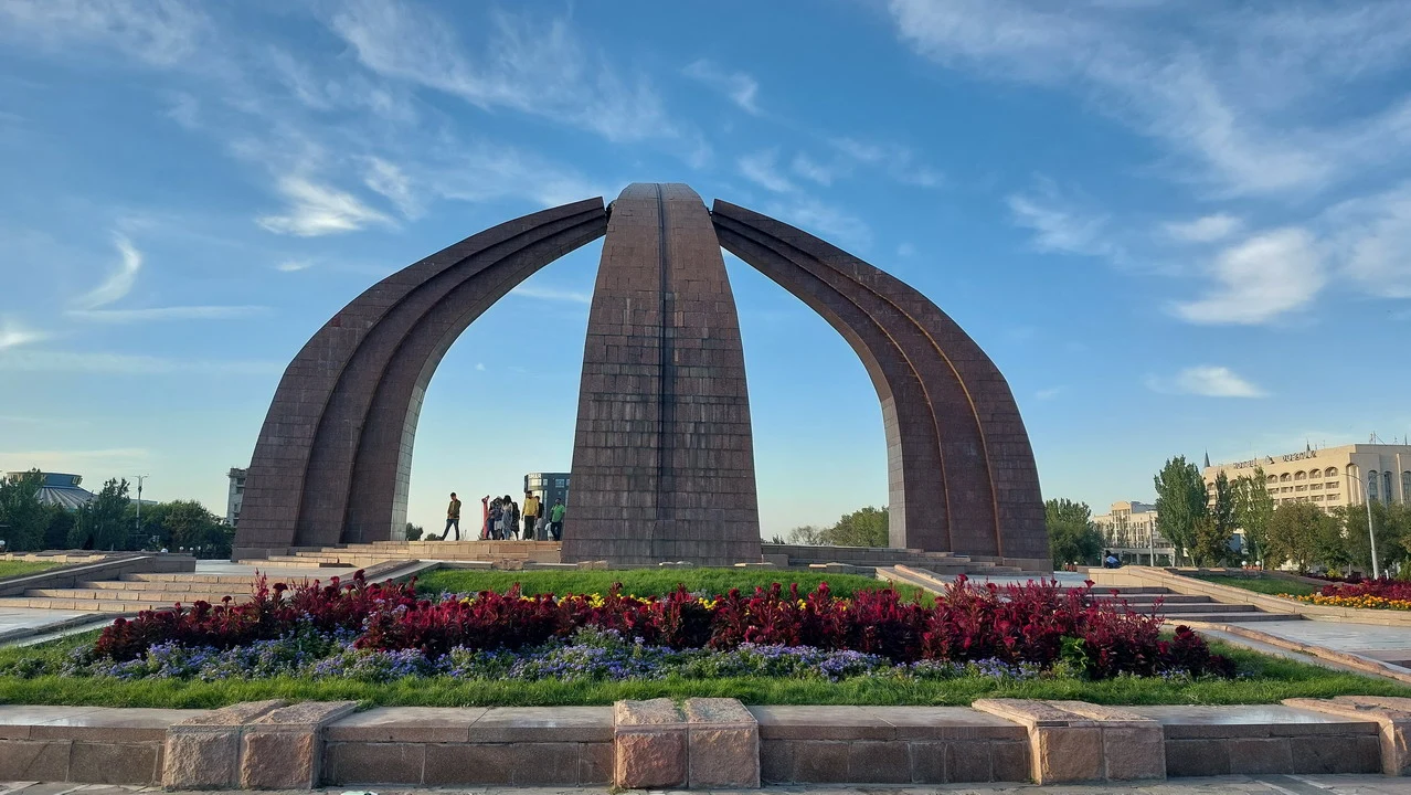 Una vista ampia della piazza della Vittoria a Bishkek con un arco monumentale in primo piano.