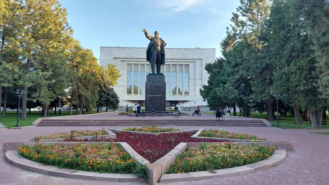 Statua di Lenin in una piazza con alberi e edifici in un contesto dell'Asia Centrale.