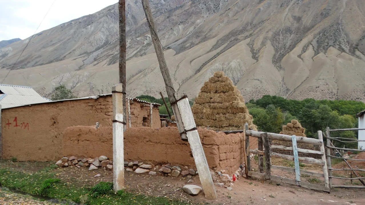 Un paesaggio rurale con una costruzione in terra battuta e un recinto di legno davanti a montagne aride.