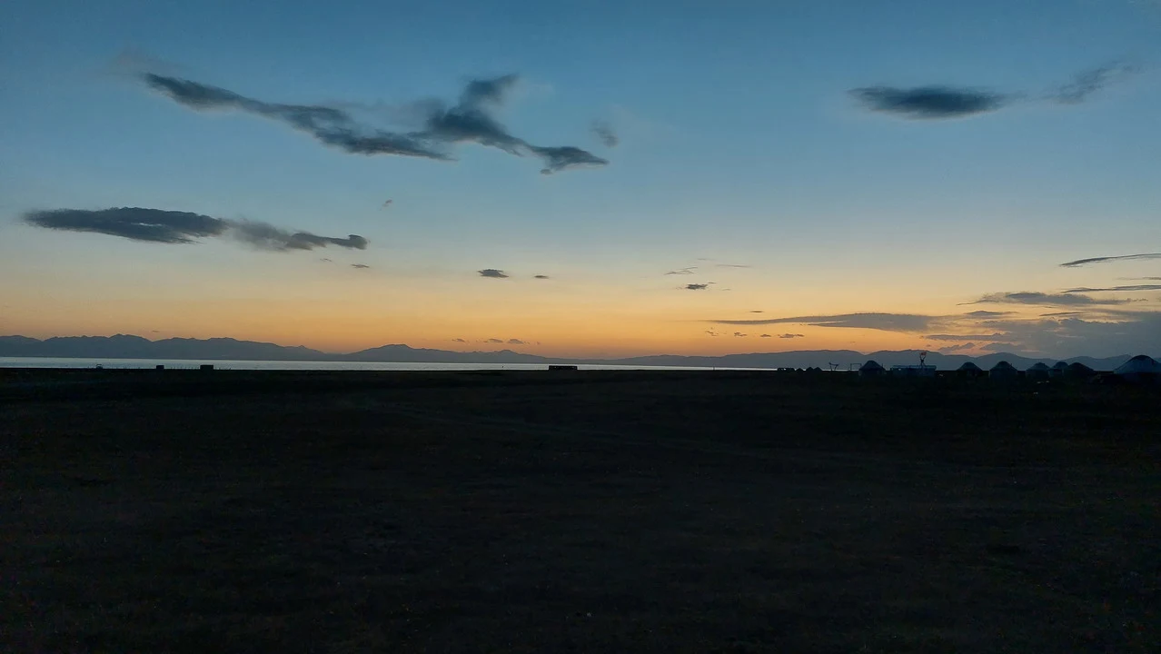 Un vasto paesaggio orizzontale al tramonto mostra un cielo con nuvole sottili sopra una linea di terra lontana.