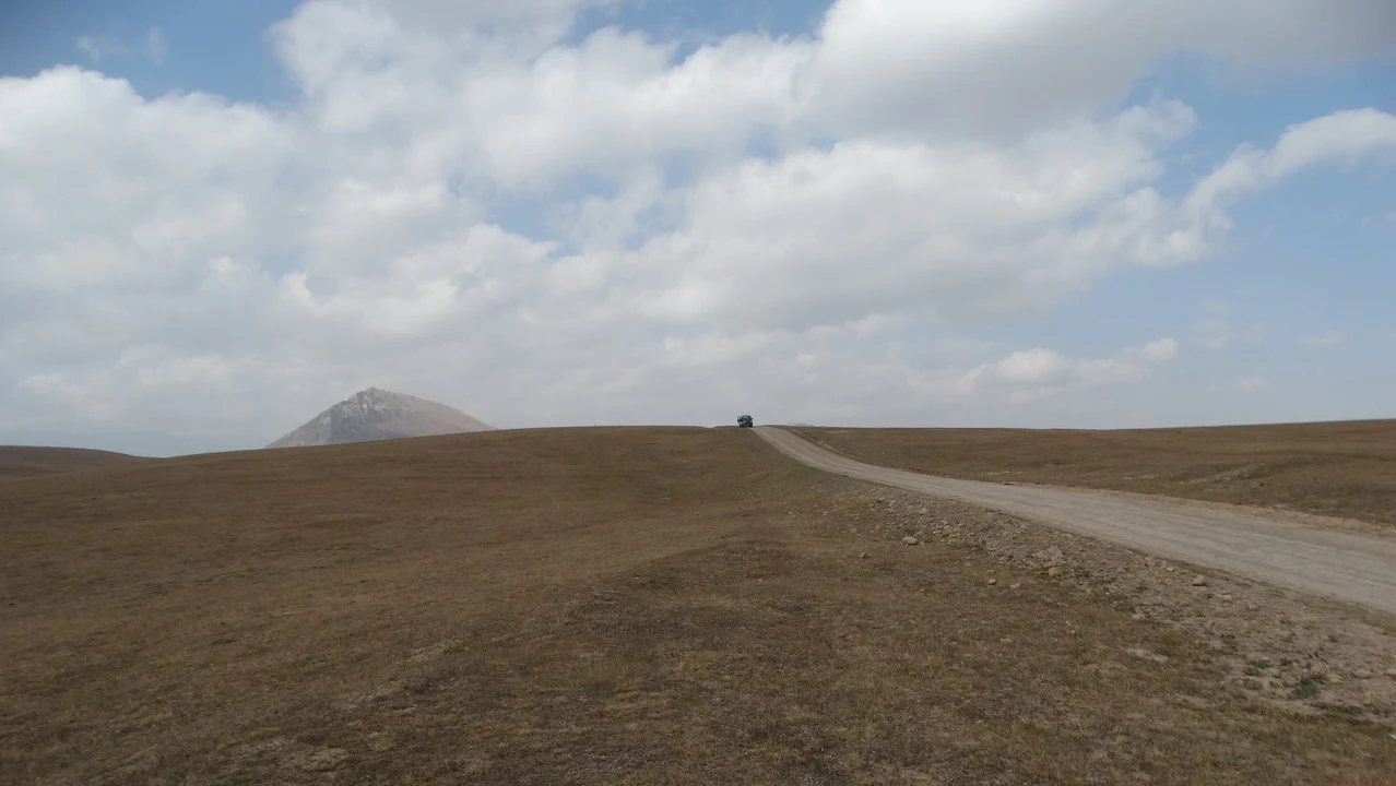 Una strada sterrata attraversa un vasto paesaggio di praterie sotto un cielo nuvoloso.