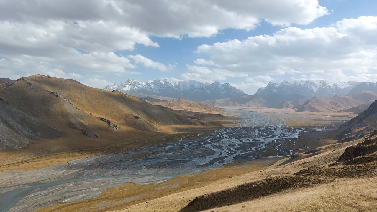 Paesaggio montano e fluviale in Asia Centrale con montagne innevate sullo sfondo.